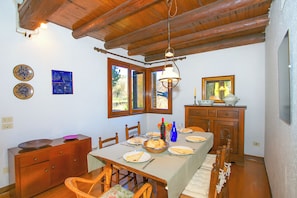 A dining area with a wooden table set for a meal, a wooden cabinet, and a window with a view of greenery. - Villa Intelvi (Cerano d'Intelvi)
