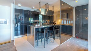 A modern kitchen with a central island, bar stools, and a glass partition. - Sant' Andrea Deluxe (Menaggio)