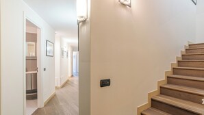 A hallway with a wooden staircase, a light switch, and a door leading to a kitchen area. - Sant' Andrea Deluxe (Menaggio)