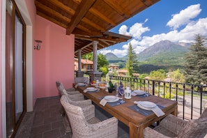 A dining area with a wooden table set for four, wicker chairs, and a view of mountains. - Villa Rosalia (Menaggio)