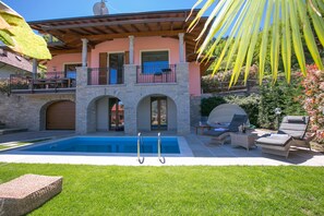 A pool with two diving boards, a covered patio area with outdoor furniture, and a stone building with a pink facade. - Villa Rosalia (Menaggio)