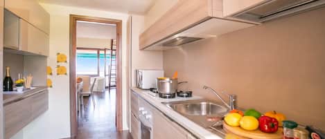A modern kitchen with a stove, sink, and a variety of fruits and vegetables on the counter.