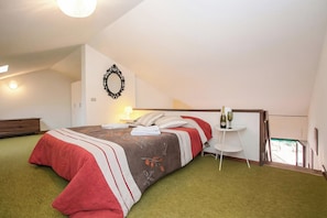 Une chambre avec un lit, une petite table sur laquelle se trouve une bouteille, une chaise et une vue sur l’extérieur.