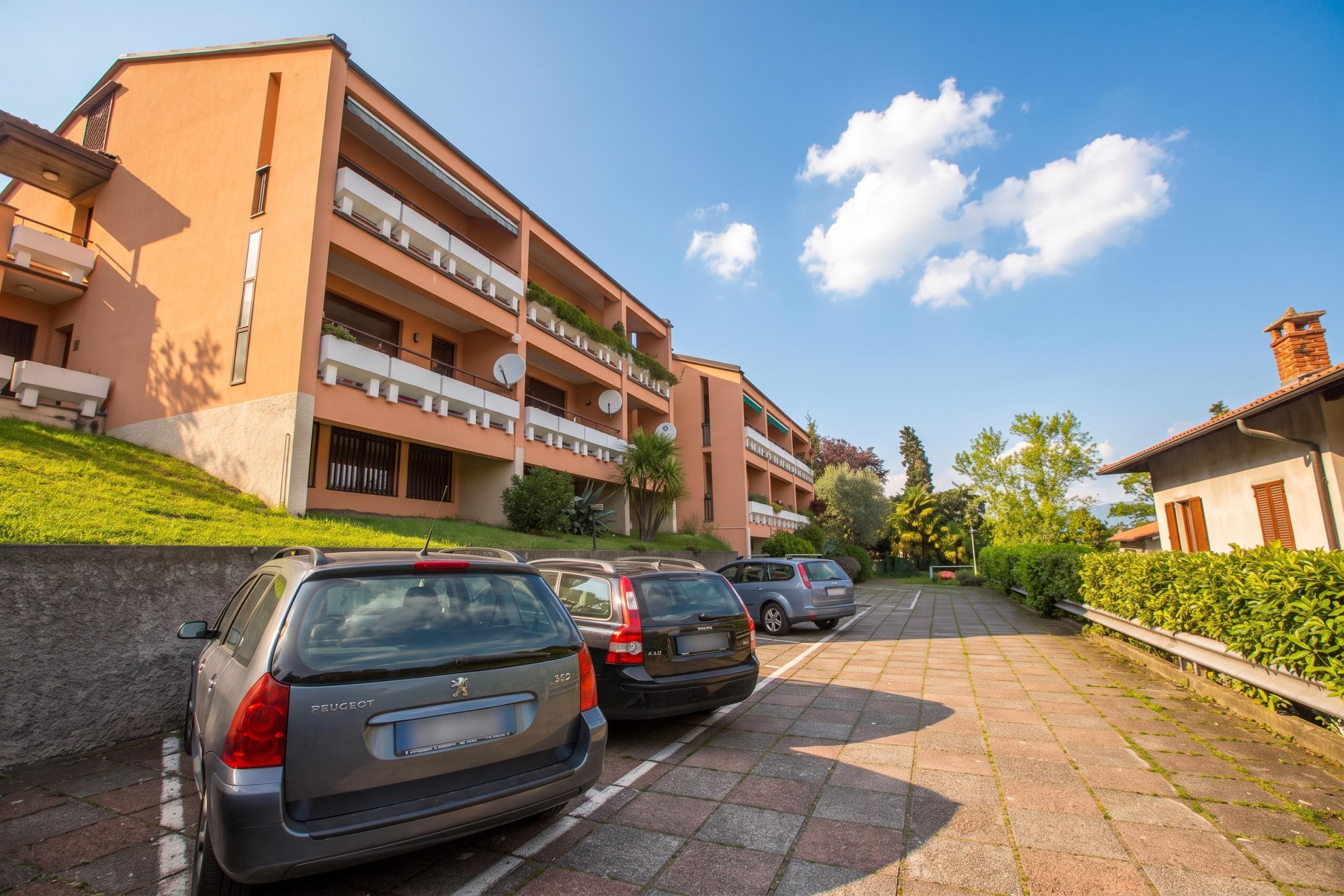 A multi-story residential building with balconies, parked cars, and a clear sky.
