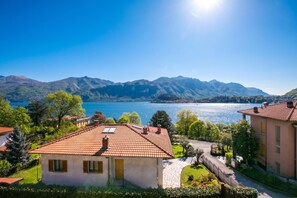 Un quartier résidentiel avec une maison dotée d’un toit en tuiles, d’un chemin en pierre et offrant une vue sur un lac, avec des montagnes en arrière-plan.