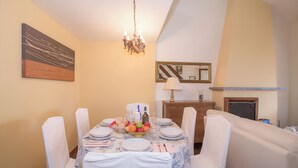 Une salle à manger avec une table dressée pour six personnes, des chaises blanches, un lustre et un miroir au mur.