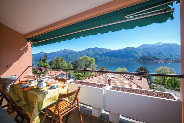Un balcón con una mesa lista para el té, con vistas a un paisaje montañoso y un cuerpo de agua.