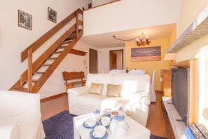 Un salon avec un escalier, un canapé blanc, une table basse avec des tasses et une théière, et un téléviseur.