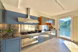 Une cuisine moderne dotée d’appareils électroménagers en acier inoxydable, d’un four encastré et offrant une vue sur un lac grâce à une porte-fenêtre coulissante.