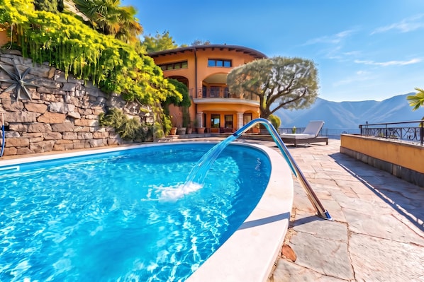 Une piscine dont l’eau est d’un bleu cristallin, entourée de murs en pierre et d’une végétation luxuriante.