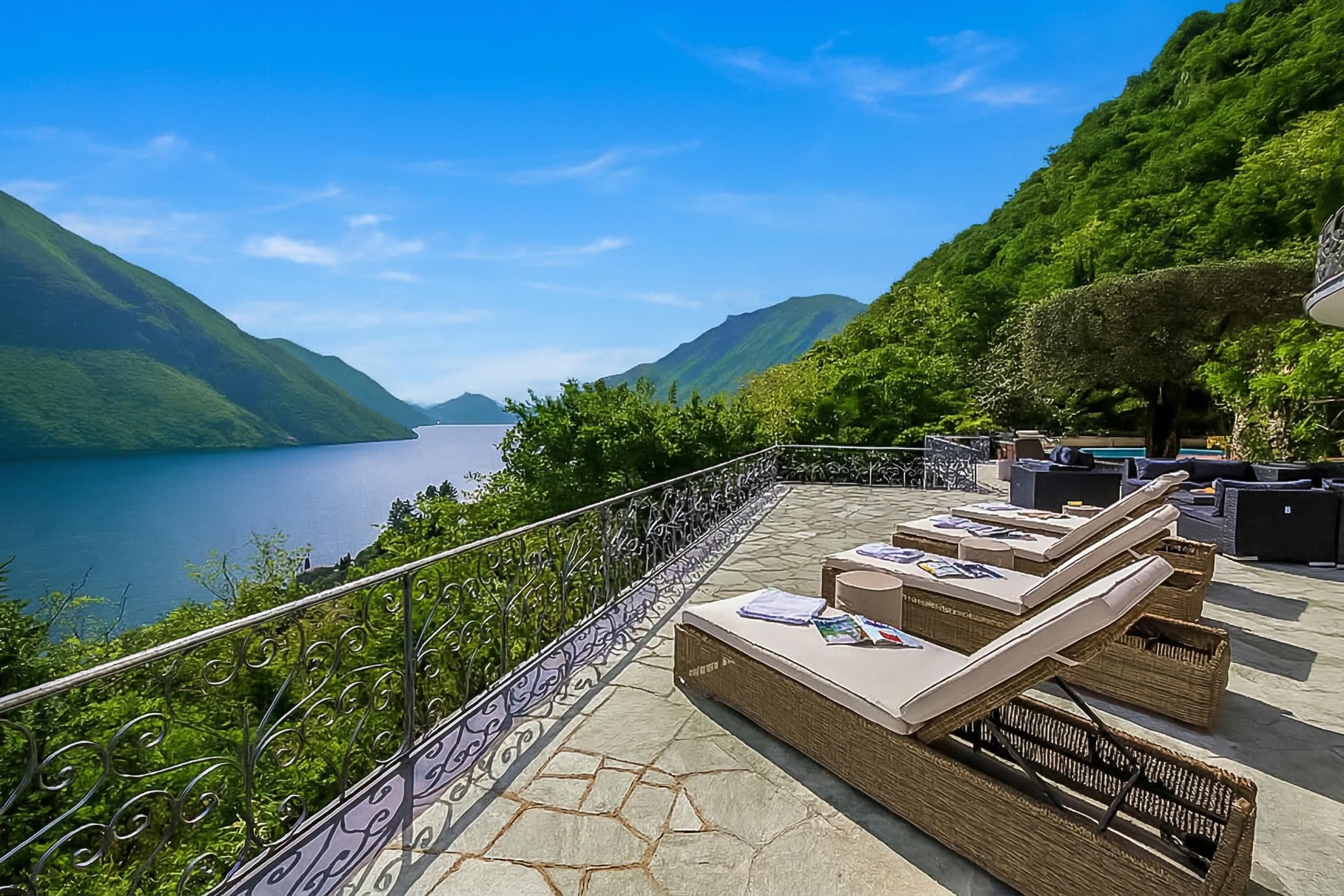 A terrace with outdoor seating, a view of a lake, and surrounding greenery.