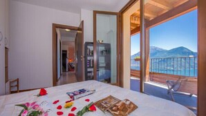 A bedroom with a bed, a balcony with a view of the sea and mountains, and a wooden ceiling. - Borgo La Sorgente - Tulipano (Gravedona)