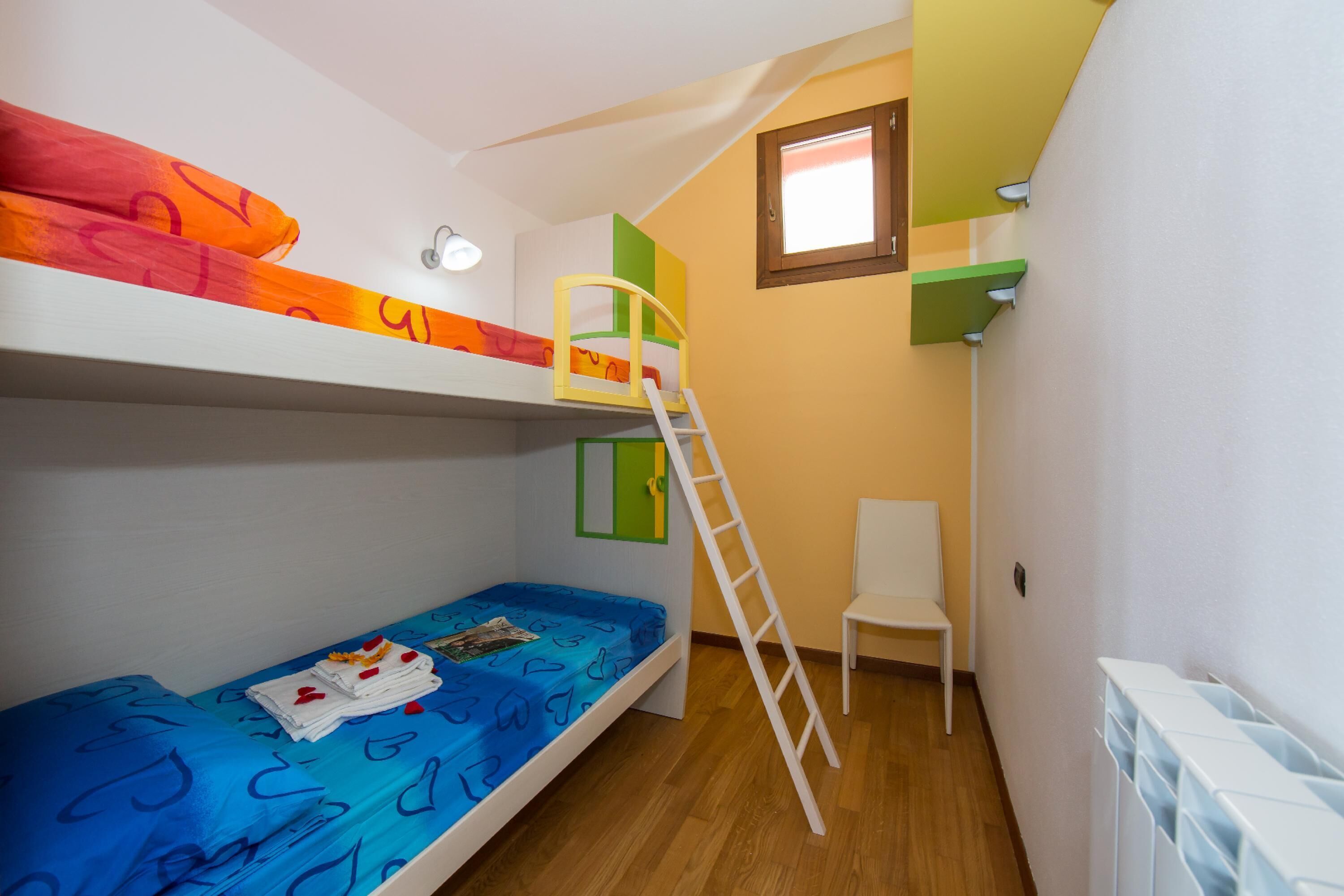 A bunk bed room with a ladder, a chair, and a window.