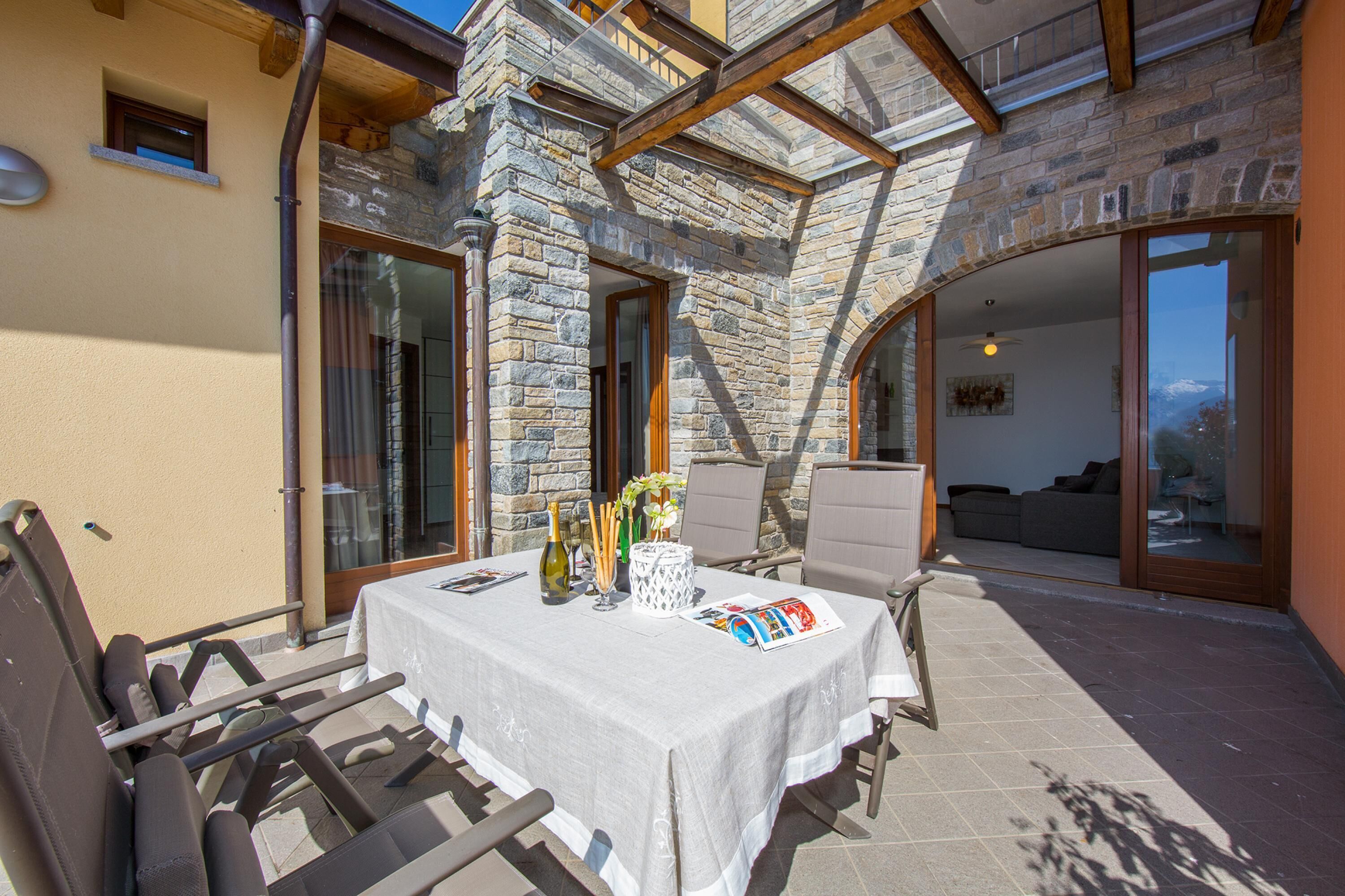 An outdoor patio with a table set for dining, stone walls, and a view of the interior.