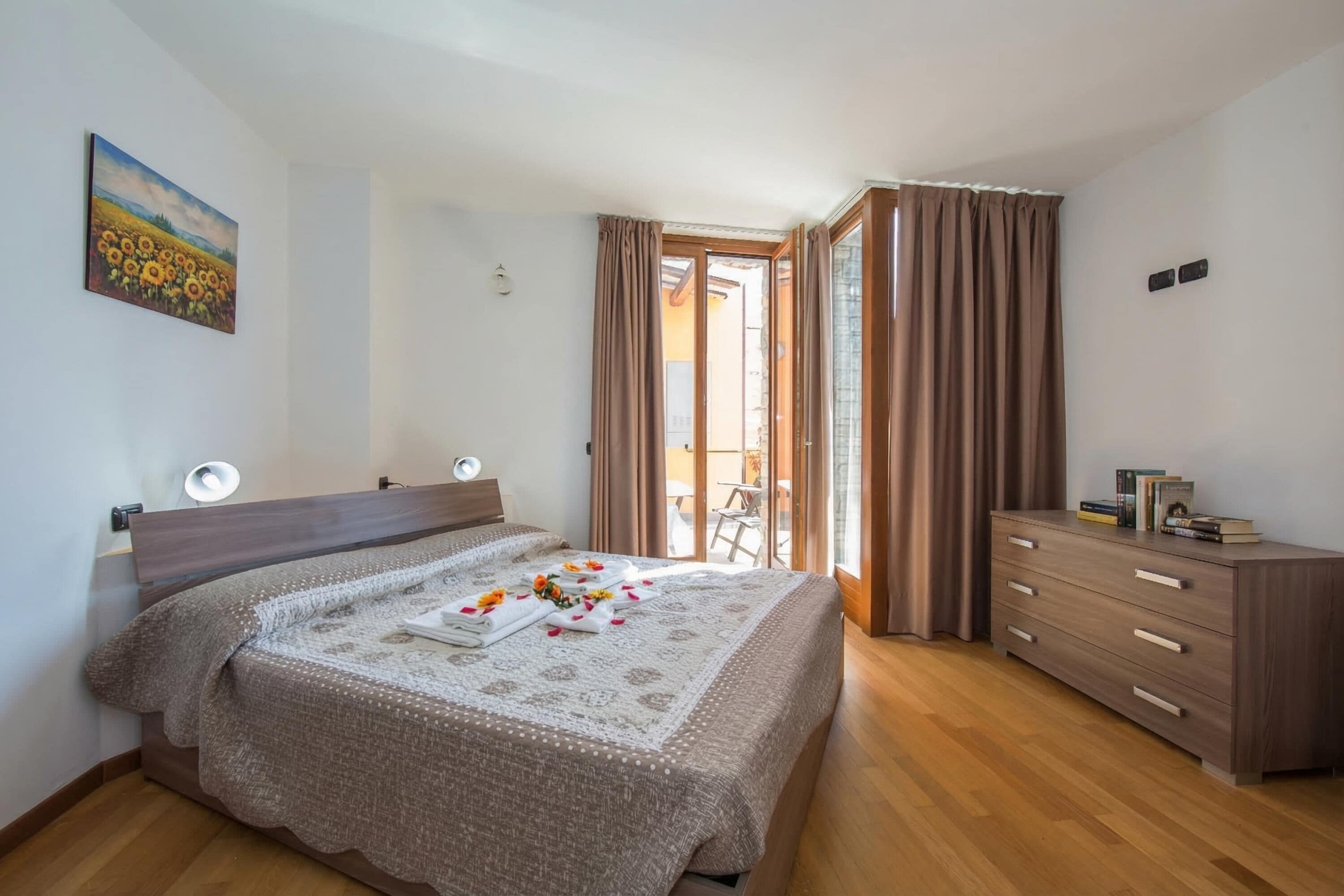 Een slaapkamer met een bed, een dressoir, een schilderij en uitzicht op het groen.