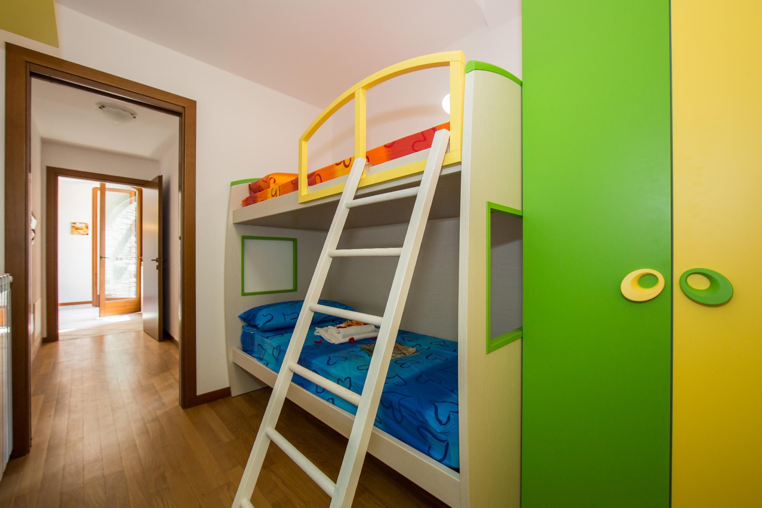 A bunk bed with a ladder, a green door, and a hallway leading to another room.