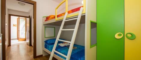 A bunk bed with a ladder, a green door, and a hallway leading to another room.