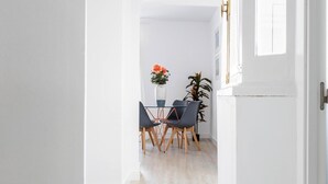 Et lyst, hvidt rum med et spiseområde, der indeholder et bord, stole, en potteplante og et vindue med udsigt.
