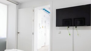 Et værelse med en hvid dør, et fladskærms-tv ophængt på væggen og en trappe i baggrunden.