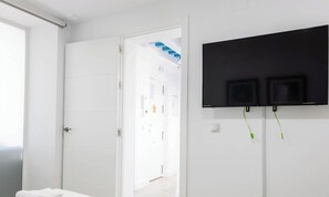 A room with a white door, a flat-screen TV mounted on the wall, and a visible door leading to another room.