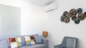En stue med en lyseblå sofa, en grå lænestol, en vægmonteret klimaanlæg og dekorativ vægkunst.
