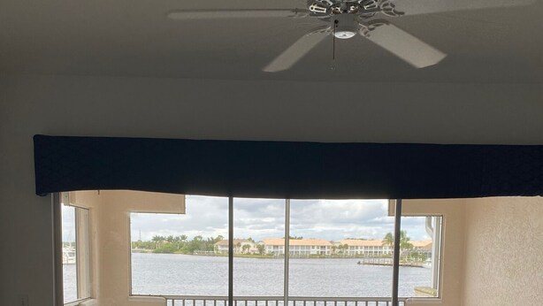 Ein Zimmer mit Blick auf ein Gewässer, einem Deckenventilator und einem Balkon mit Tisch und Stühlen.