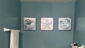 Ein Badezimmer mit einer Badewanne, zwei Handtüchern, die an Handtuchhaltern hängen, und drei gerahmten Kunstwerken an der Wand.