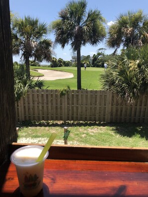 A view of a golf course with a wooden fence, palm trees, and a drink on a table. - Spacious Hilton Head Resort Condo/Villa Near Beach (Hilton Head Island)