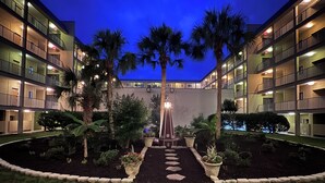 Un hotel de varios pisos con un patio central que presenta palmeras, un camino y un farol decorativo.