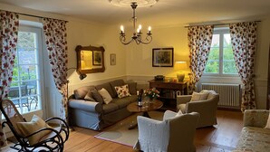 Ein gemütliches Wohnzimmer mit einer Couch, Sesseln, einem Esstisch mit Lampe und einem Chandelier.