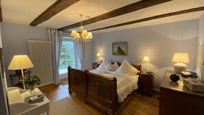 Ein Schlafzimmer mit einem hölzernen Bett, zwei Nachttischen mit Lampen, einem Heizkörper, einem Fenster mit Vorhängen und einer Deckenleuchte.