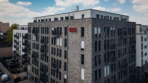 Un immeuble à plusieurs étages, doté d’une façade en pierre, de nombreux balcons et d’une enseigne indiquant qu’il s’agit d’un complexe résidentiel.