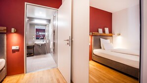 Une chambre d’hôtel comprenant un lit, une table de chevet, un miroir et une petite salle de bain avec un lavabo et un porte-serviettes.