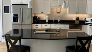 Una cocina moderna con armarios blancos, electrodomésticos de acero inoxidable y una isla central con taburetes de bar.
