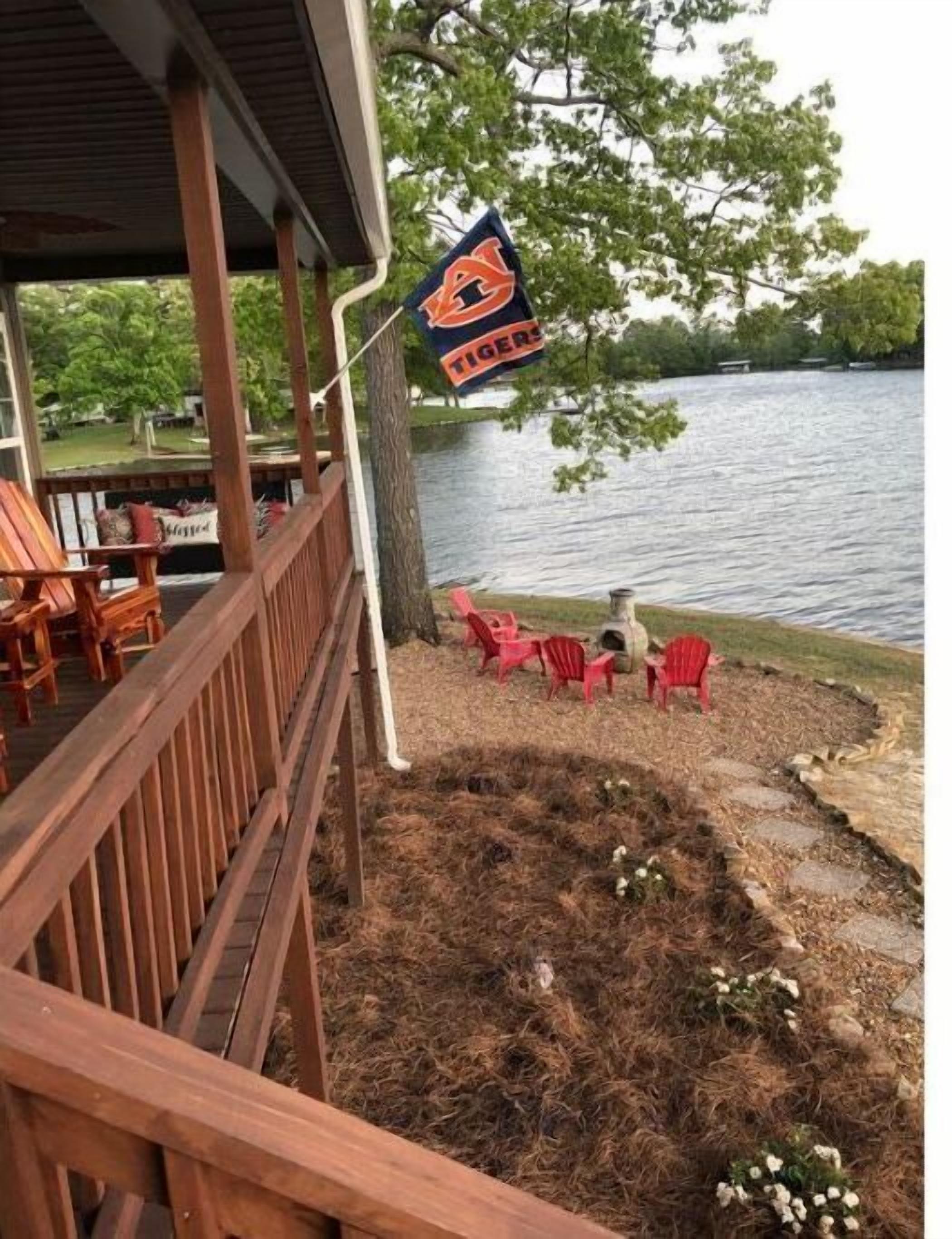 A covered deck with wooden railings, a flag, and red chairs by a lake.
