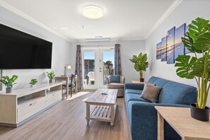 A modern living room with a flat-screen TV, a blue sofa, a wooden coffee table, and potted plants. - MONTHLY RENTAL - Gorgeous Modern Ocean View Condo w/ Access to Resort Amenities (Myrtle Beach)