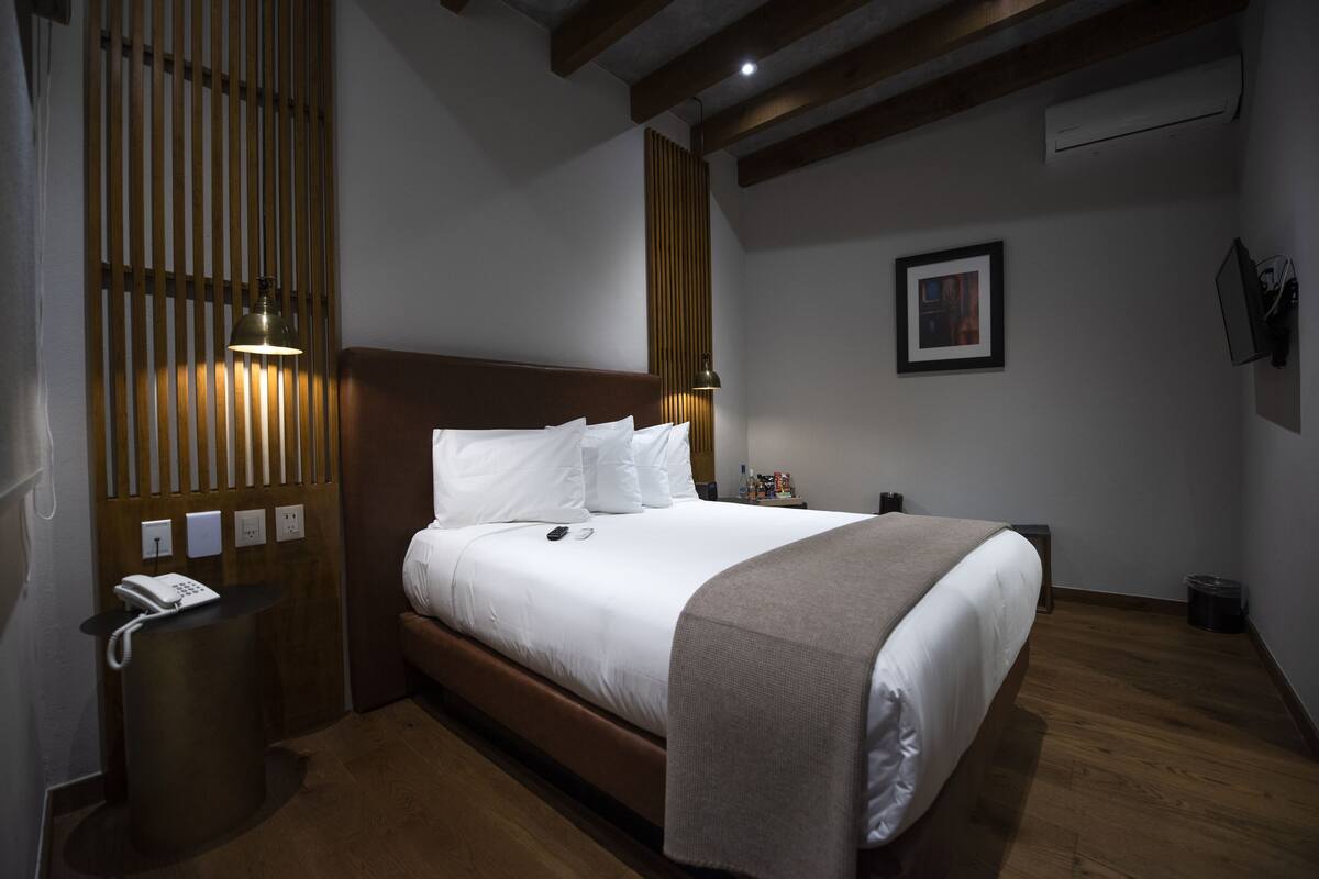 Habitació d'hotel amb un llit de fusta, una taula de nit amb una làmpada, un telèfon i un quadre a la paret.