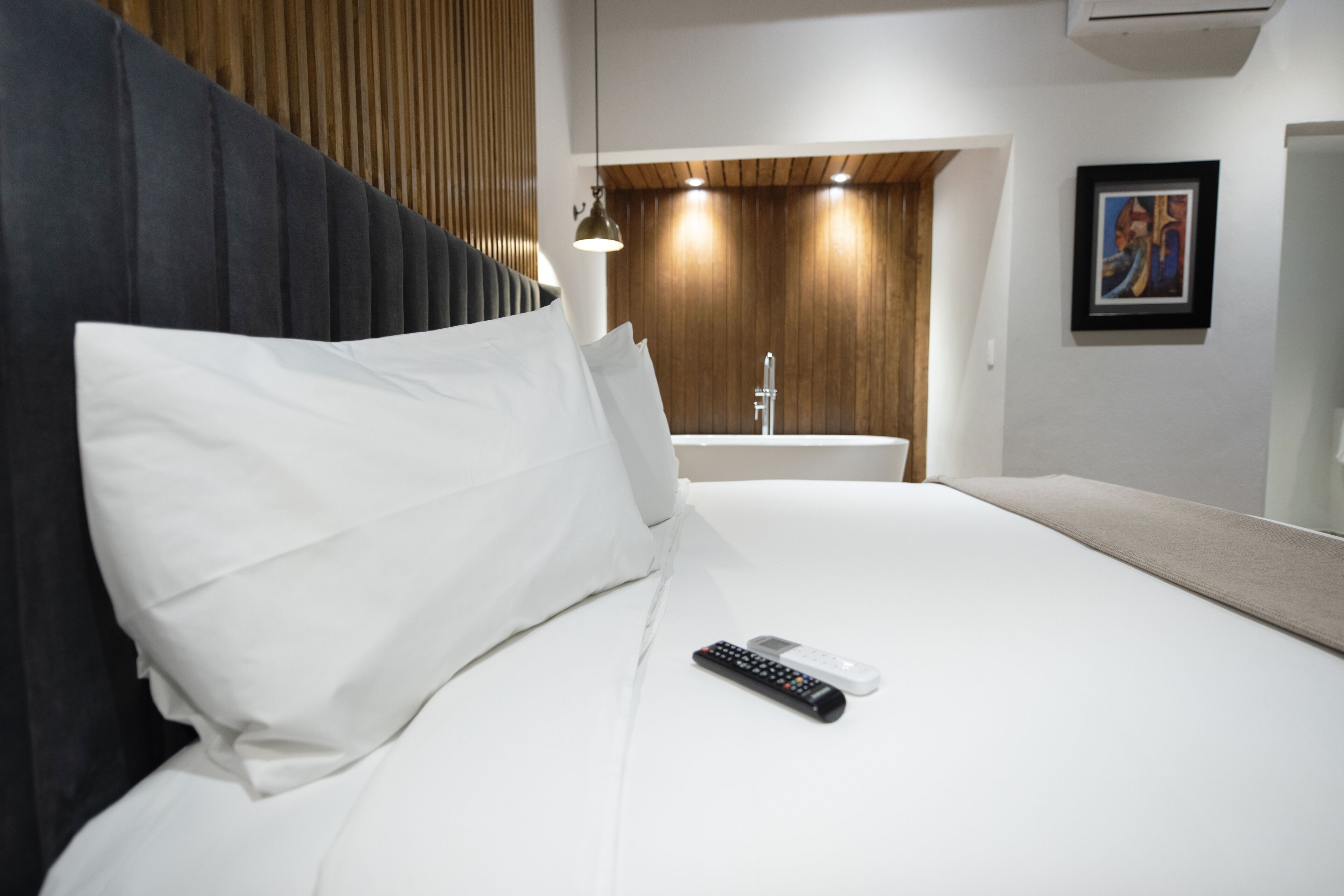 Une chambre d’hôtel avec un lit, une télécommande, un lavabo et un tableau encadré au mur.