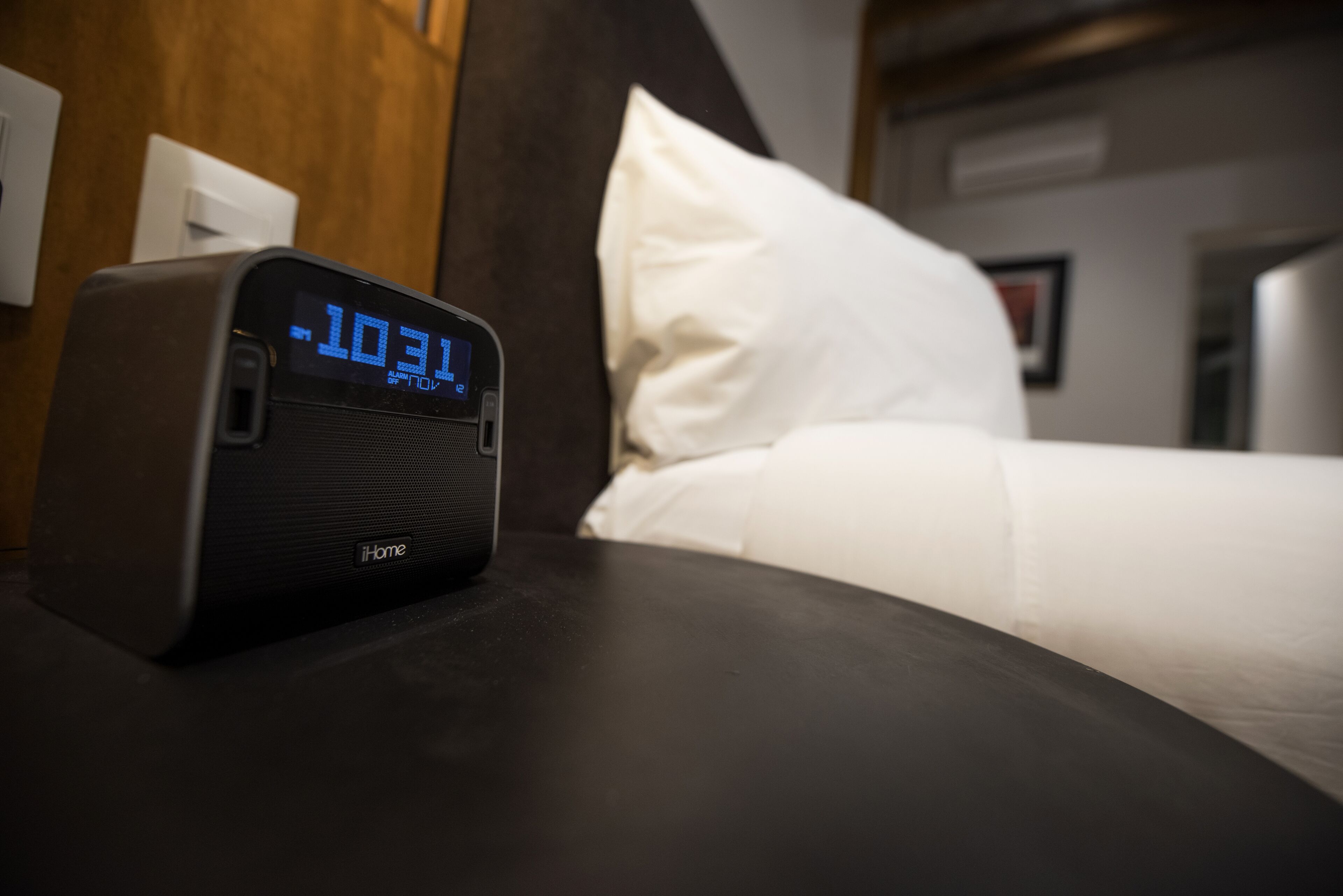 A digital clock displaying the time on a bedside table in a hotel room.