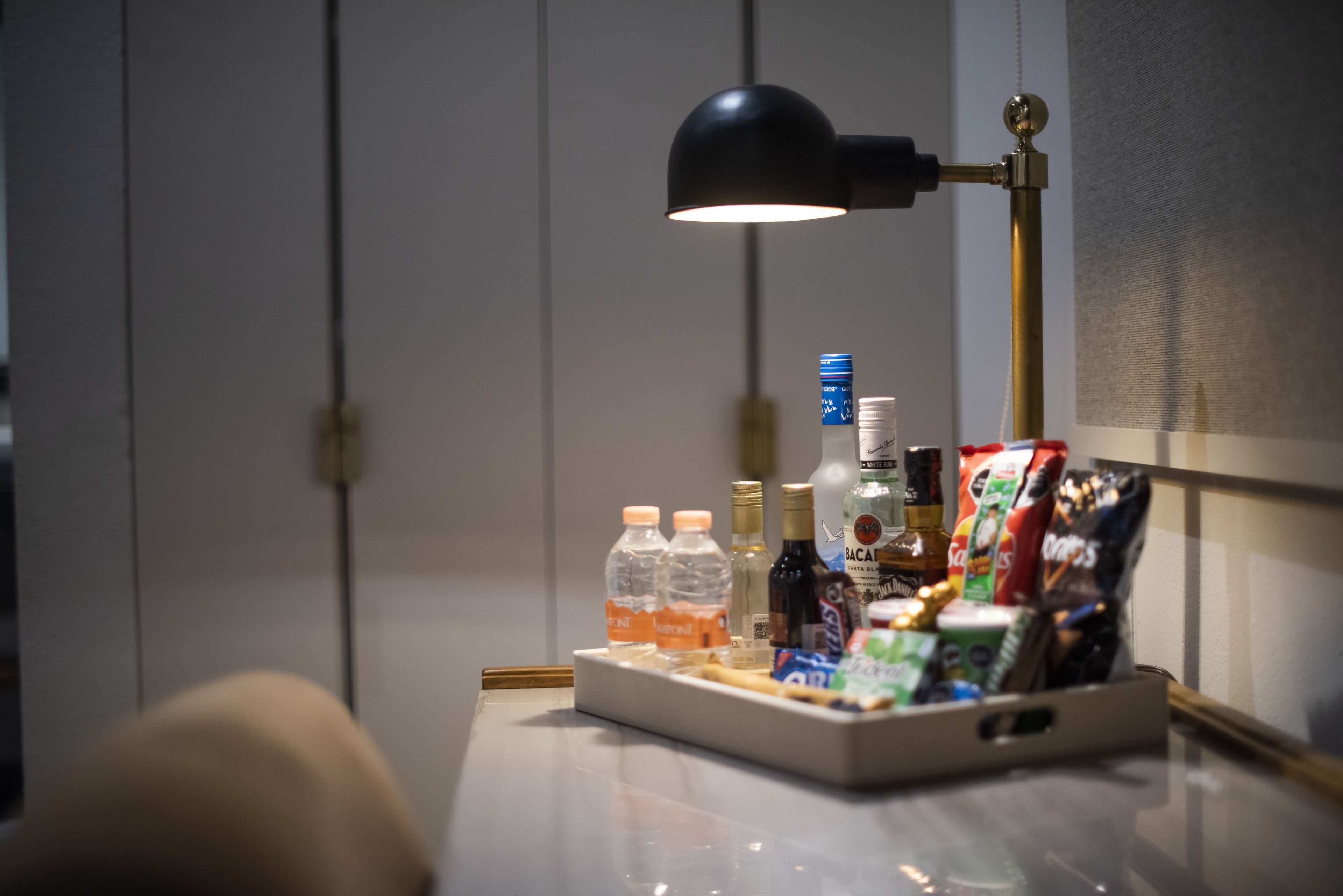 Un bureau avec une lampe, des bouteilles, des en-cas et un plateau.