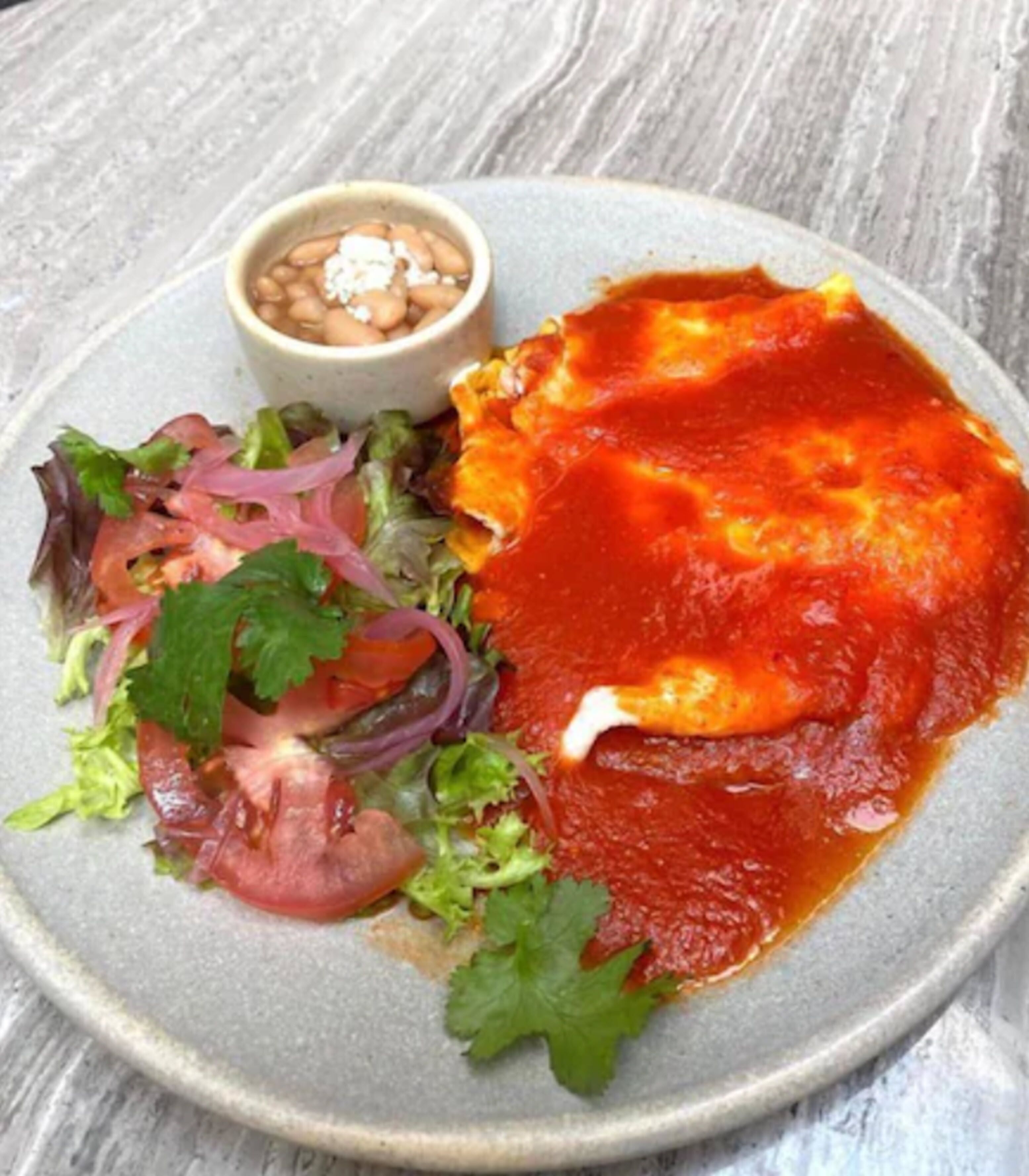 Un plato con salsa roja, una ensalada y un tazón pequeño de frijoles.