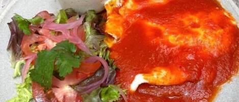 Un plato con salsa roja, una ensalada y un tazón pequeño de frijoles.