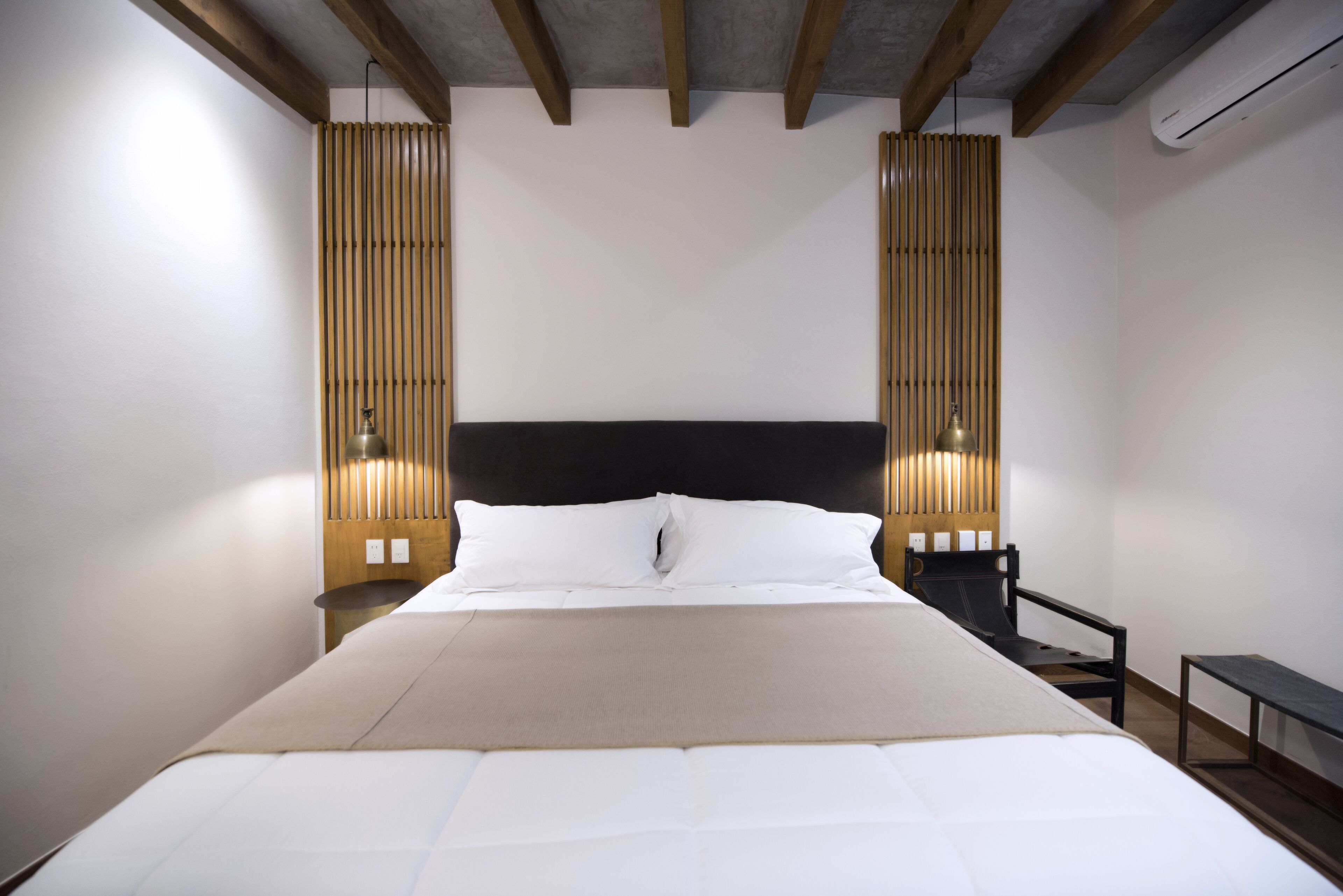 A modern hotel room with a large bed, wooden slats on the walls, and a simple nightstand with a lamp.