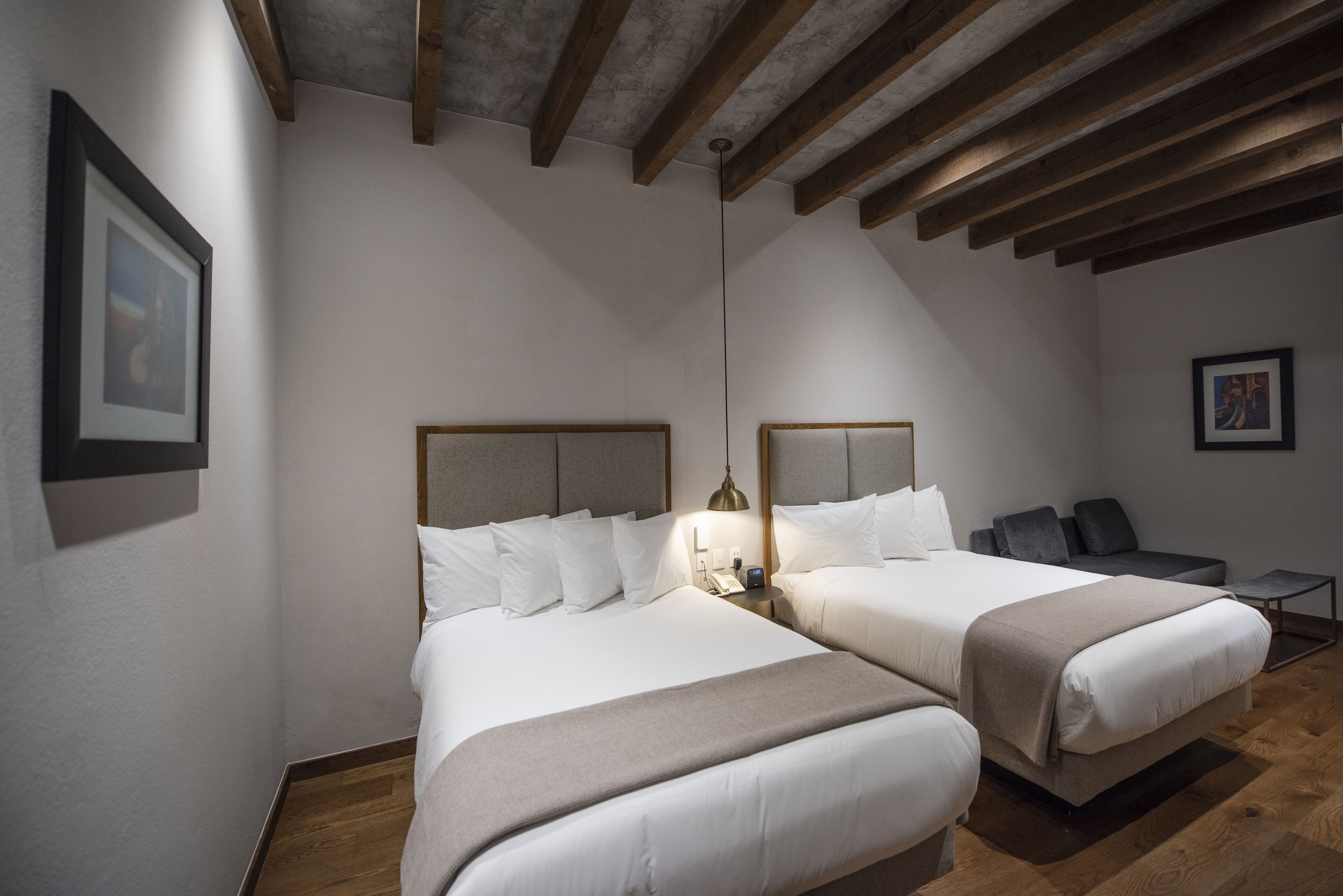A hotel room with two beds, a nightstand, a lamp, and a small table.