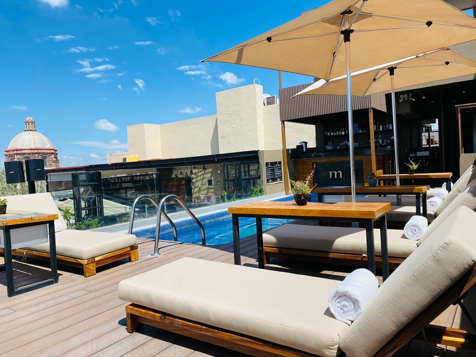 A rooftop pool area with lounge chairs, a bar, and a view of a historic building.