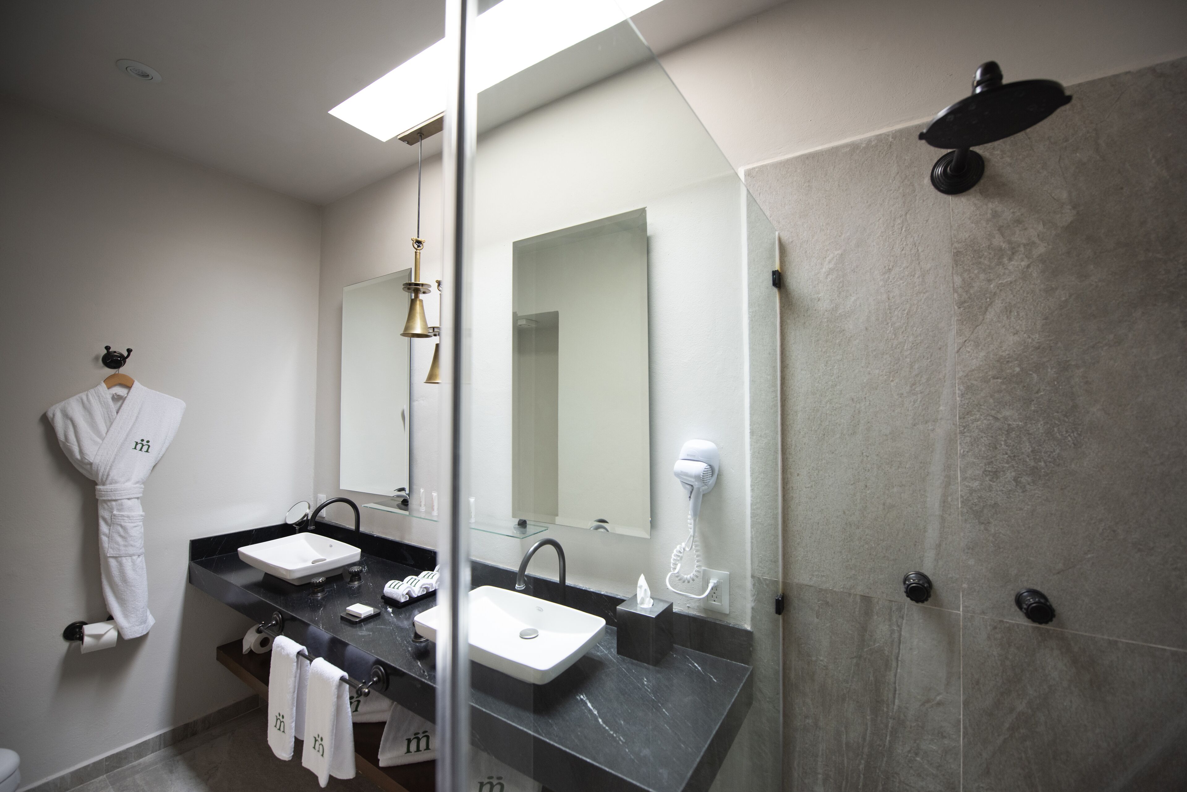A modern bathroom with two sinks, a large mirror, a hairdryer, and a robe hanging on the wall.