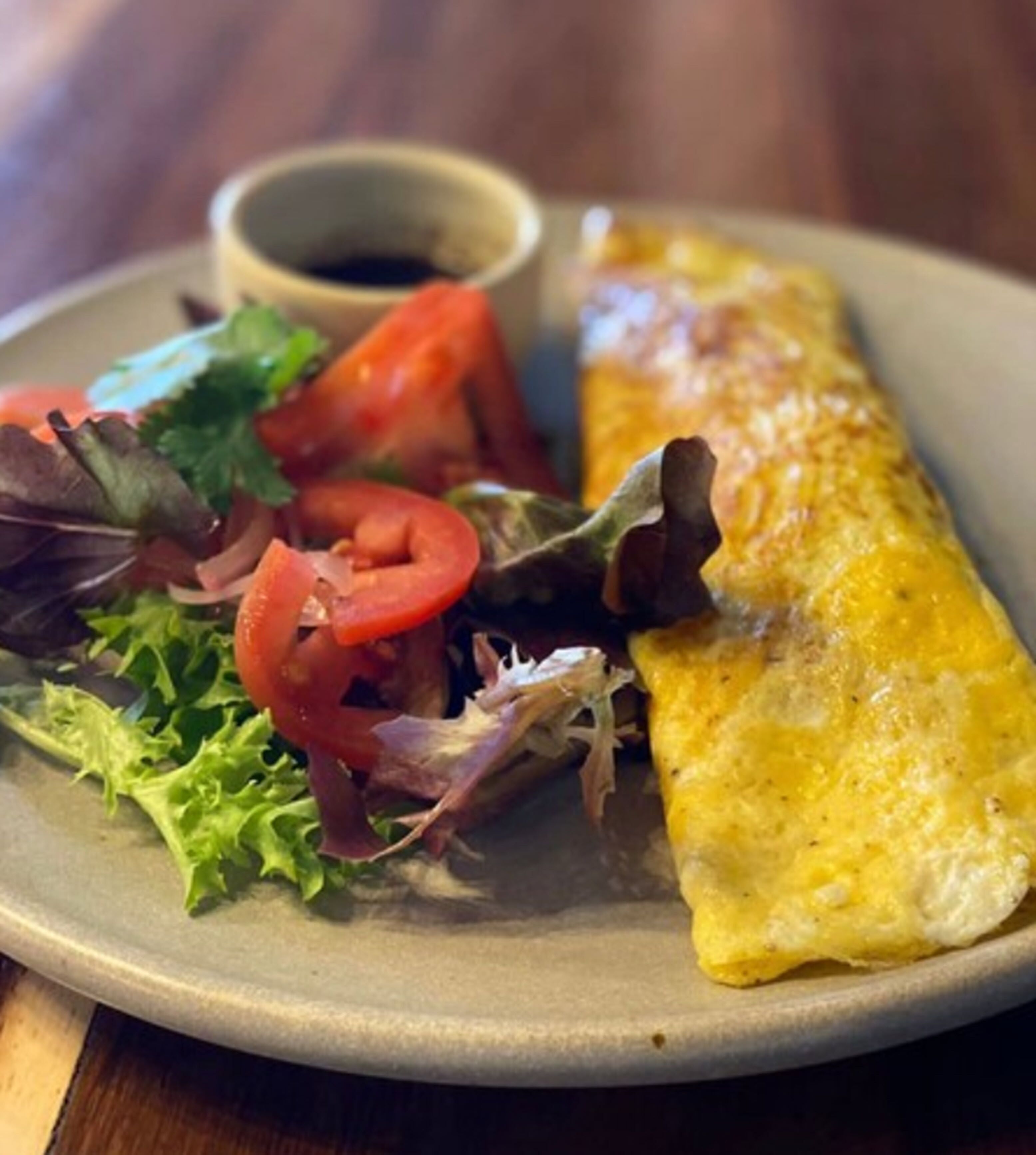 A plate with a rolled omelette, a small bowl of sauce, and a side salad.