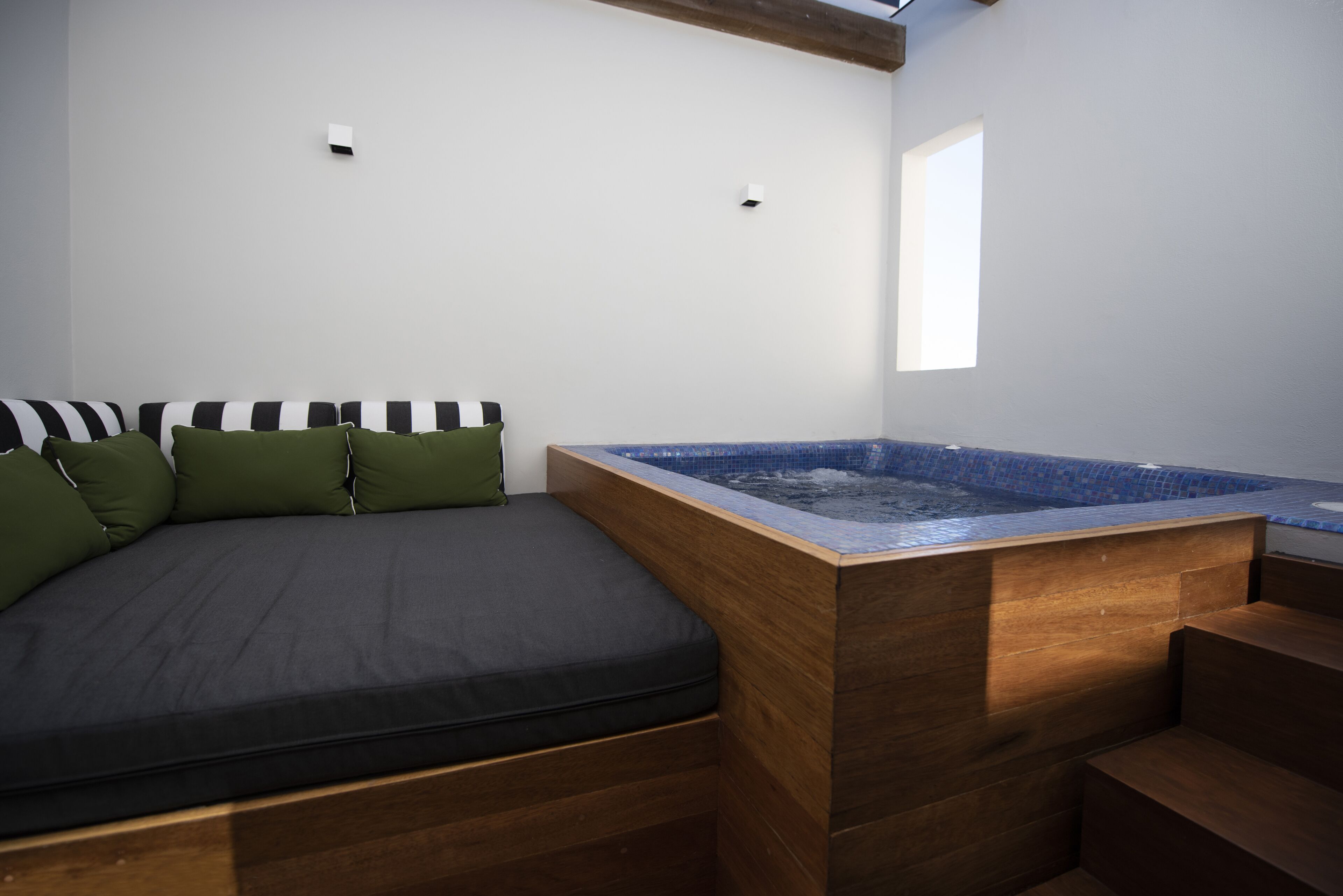 A modern room with a wooden bench, a small hot tub, and a bed with striped pillows.
