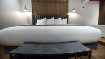 A large bed with a grey headboard and white bedding, two pendant lights, and a wooden floor.