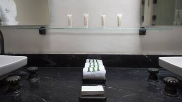 A bathroom with a black marble countertop, a glass shelf holding four tubes, and a towel rack with a towel.
